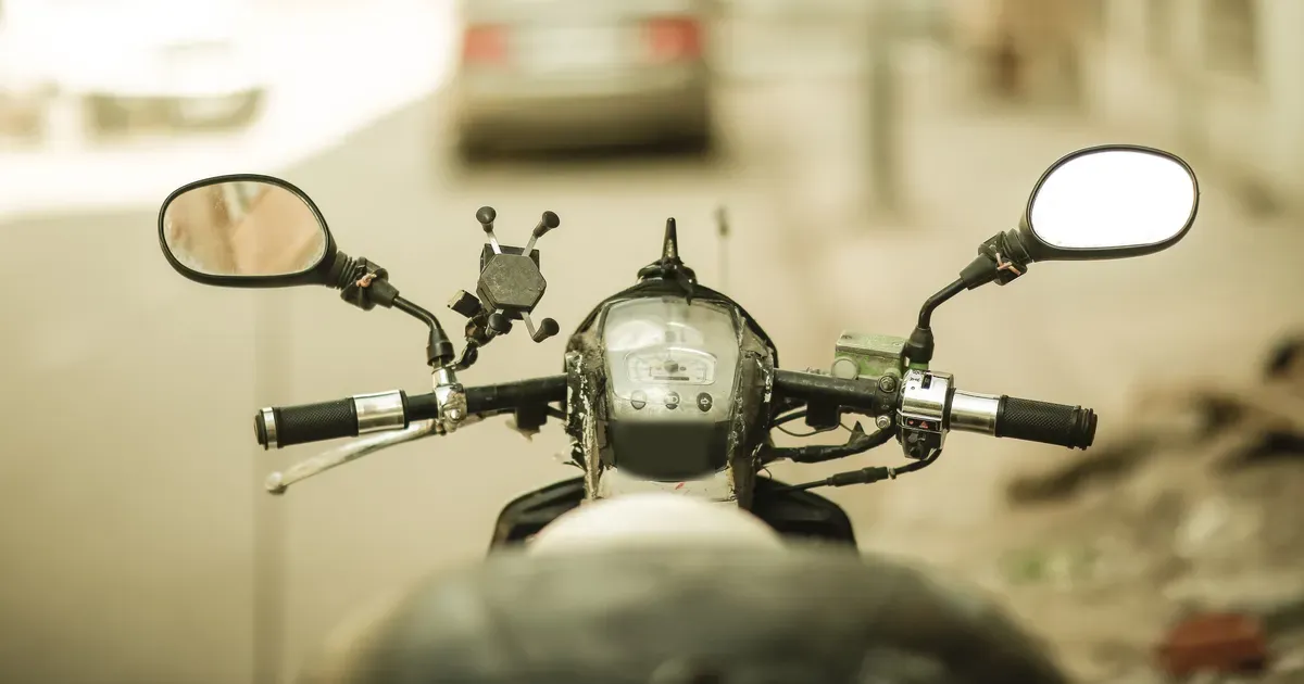 Stuur en spiegels van een motor, met een wazige auto op de achtergrond