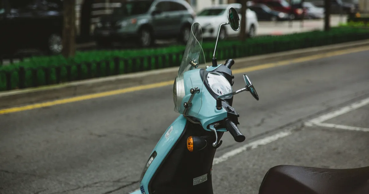 Een lichtblauwe scooter staat geparkeerd langs een stadsweg